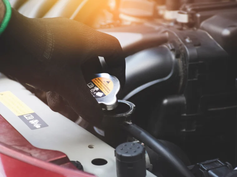 Mechanic hand opening a radiator cap to check the coolant level of the car radiator.